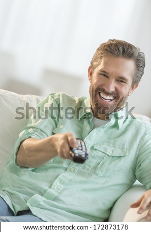 Cheerful mature man watching TV on sofa in living room
