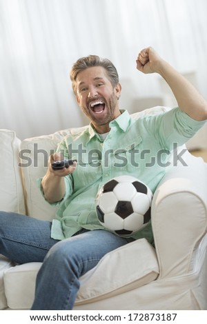 Excited mature man cheering while watching soccer match on sofa at home