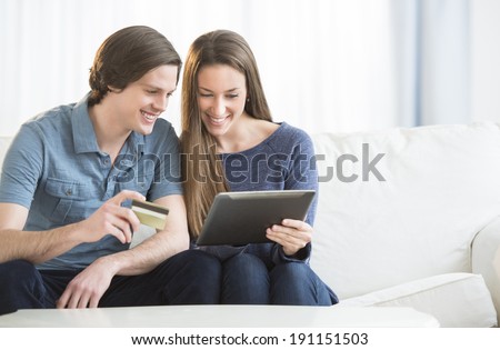 Happy young couple using credit card while shopping online on digital tablet in living room