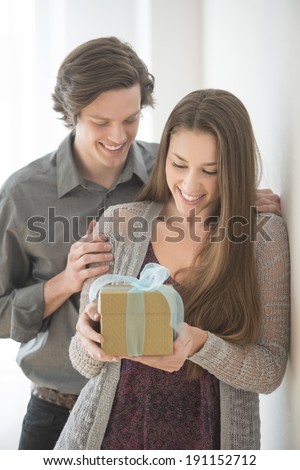 Smiling young man giving birthday present to woman at home