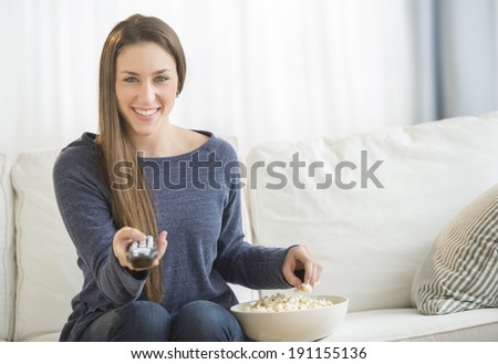 Portrait of beautiful young woman eating popcorn while watching TV in living room