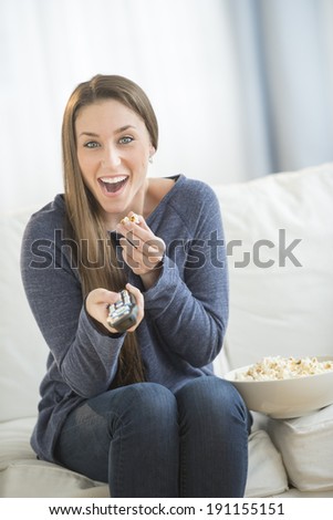 Portrait of happy young woman eating popcorn while watching TV in living room