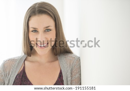 Portrait of confident young woman leaning on wall at home