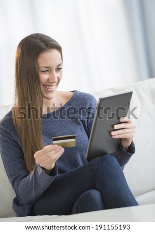Beautiful young woman with credit card shopping online on digital tablet in living room