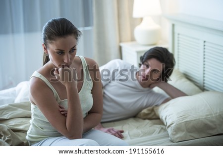 Depressed young woman looking away with man in background on bed