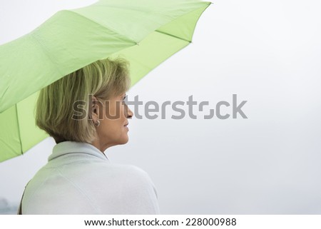 Rear view of mature woman with green umbrella looking away against clear sky