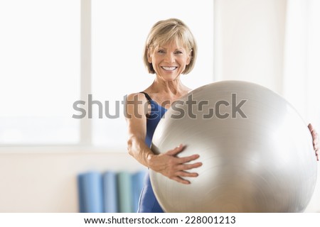 Portrait of happy mature woman holding yoga ball at home