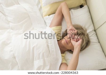 High angle view of mature woman rubbing eyes while lying in bed at home