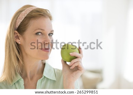 Portrait of beautiful mature woman holding granny smith apple at home