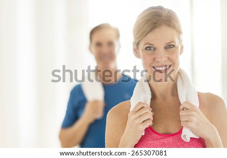 Portrait of fit mature woman holding towel around neck with man in background at home