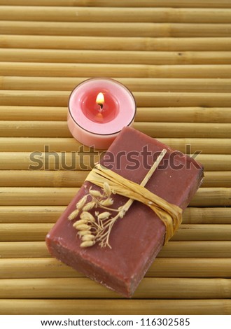 Bar of natural handmade soap with candle on wooden mat.