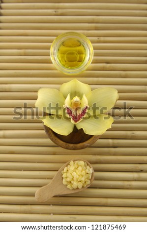 Yellow orchid in bowl and massage oil, salt in spoon on mat