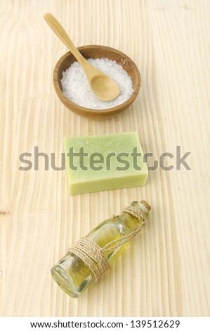 Salt on bowl ,green soap , spoon, massage oil on a wooden board