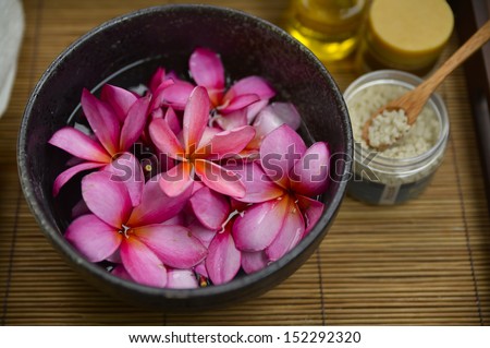 Many red frangipani in bowl , candle ,salt in bowl, oil on bamboo mat