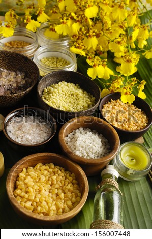 wooden bowl of color sea salt with ,candle ,massage oil and branch yellow orchid on leaf
