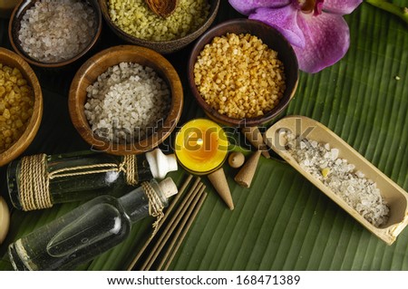 wooden bowl of color sea salt with ,candle ,massage oil and orchid on banana leaf