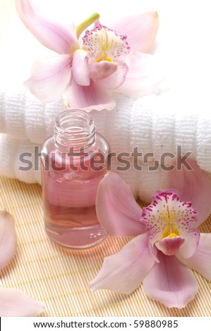 Pink orchid on spa towel and perfume bottles on straw napkin