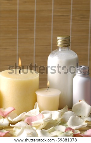Body oils, rose petals and candle on bamboo stick straw mat background