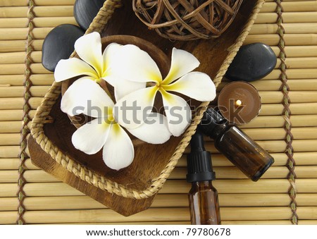 White frangipani and massage oil and candle in a bowl on mat
