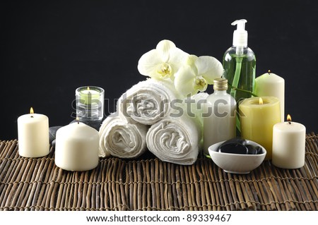 Three roller towel with massage oil .candle ,bowl of stones, orchid All on the bamboo mat.