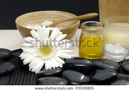gerbera with massage oil and herbal salt in spoon on bowl and stones