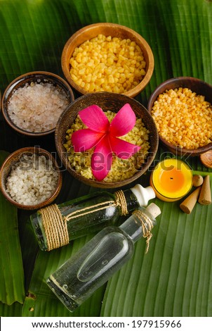 Red frangipani and massage oil with candle ,salt in bowl on green banana leaf