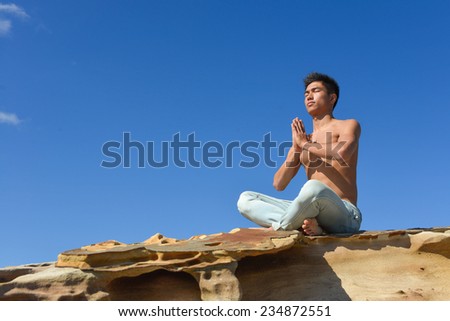 Young man meditating sitting on a rock