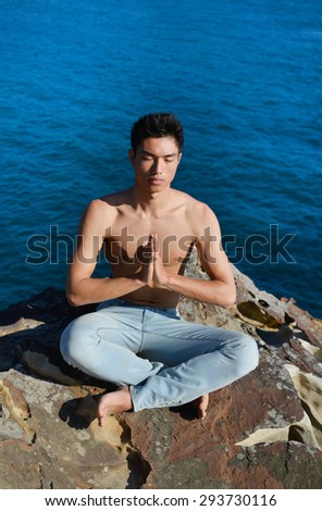 male model doing yoga sitting back on rocks at beach