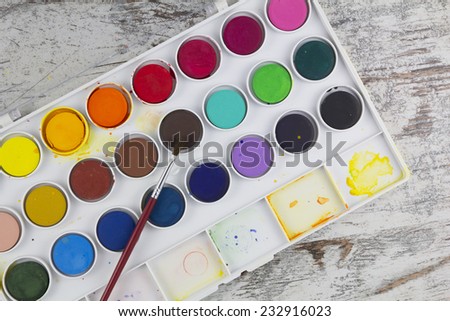 Watercolor palette with paintbrush in a wood background