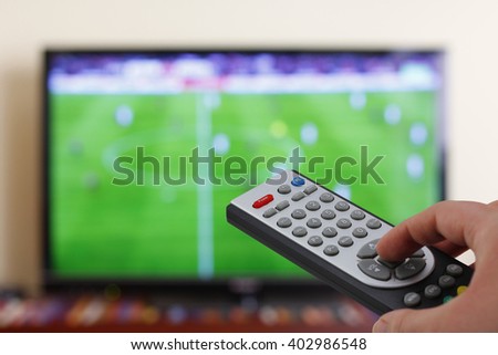 Watching a football match in the television, with a tv remote control in the hand