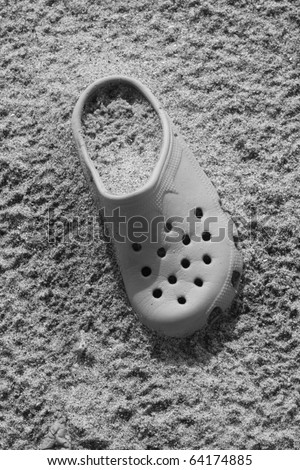 Old crock shoe semi buried in beach sand (black and white photo)