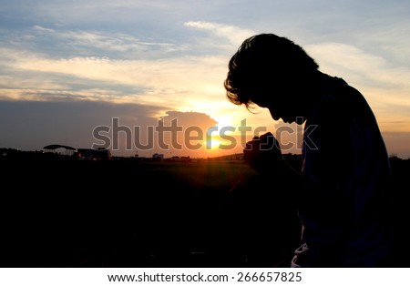 Silhouette of man praying over beautiful sunset background