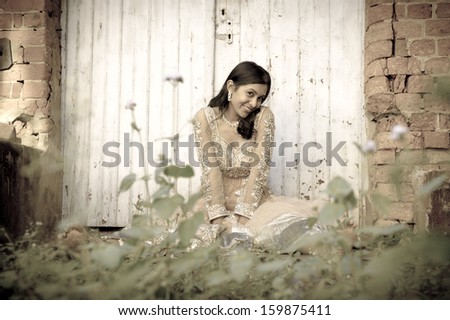 Young attractive indian woman sitting by white double doors in garden