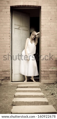 Young attractive caucasian woman leaning against door frame wearing white dress