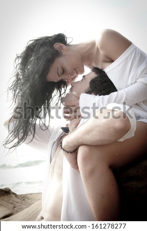 Young attractive couple kiss on rocks beach wearing white kissing love passionate