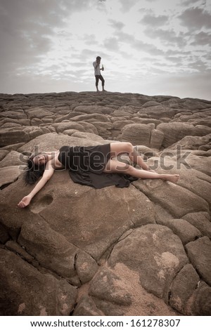 Young attractive caucasian woman lying on rocks with clouds overhead and man in background