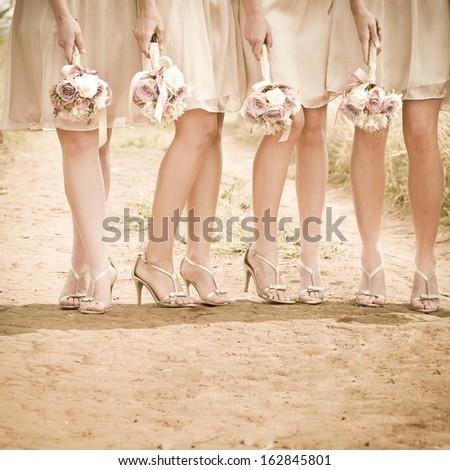 Group of young women wearing heels with bouquets of flowers standing on dirt road
