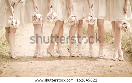 Group of young women wearing heels with bouquets of flowers standing on dirt road