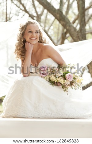 Young attractive bride sitting with bouquet of flowers smiling while looking away from camera