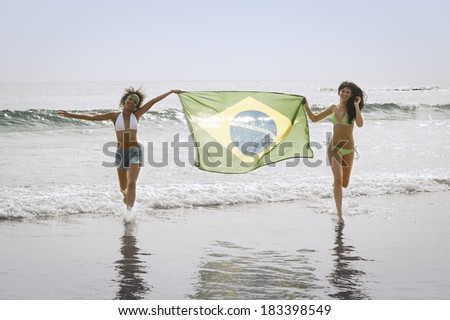 Two young football supporters running though surf with Brazil flag