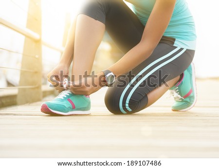 Young runner tying shoe lace on wooden boardwalk at sunrise