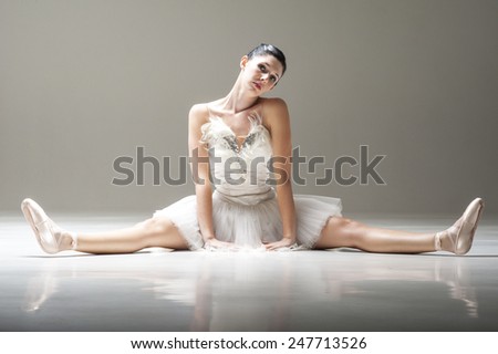 Young beautiful ballerina sitting stretching under spotlight in costumed tutu