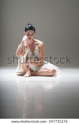 Young beautiful ballerina sitting under spotlight with pointed ballet shoes