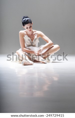 Young beautiful ballerina sitting on floor putting on her ballet shoes