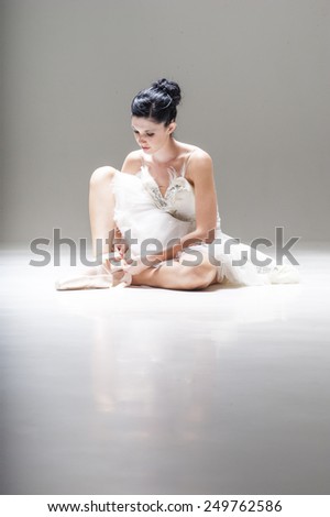 Young attractive ballerina sitting lacing up ballet shoes