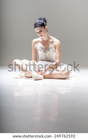 Young attractive ballerina sitting lacing up ballet shoes