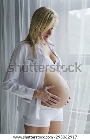 Young pregnant woman standing at window with unborn child