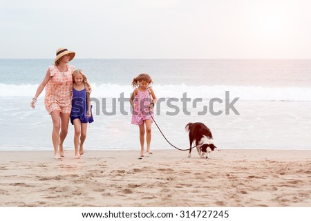 2 girls walking on beach with mom and dog. Happy family walking.