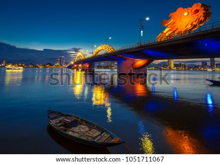 Dragon Bridge in DaNang all lit up, taken in the evening just after sunset. The bridge and city lights reflecting on the large river.