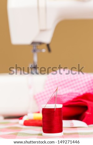 Red thread reel with an out of focus sewing machine and colorful cloths in the background